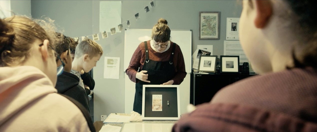 Person holding small artwork to a class of children.