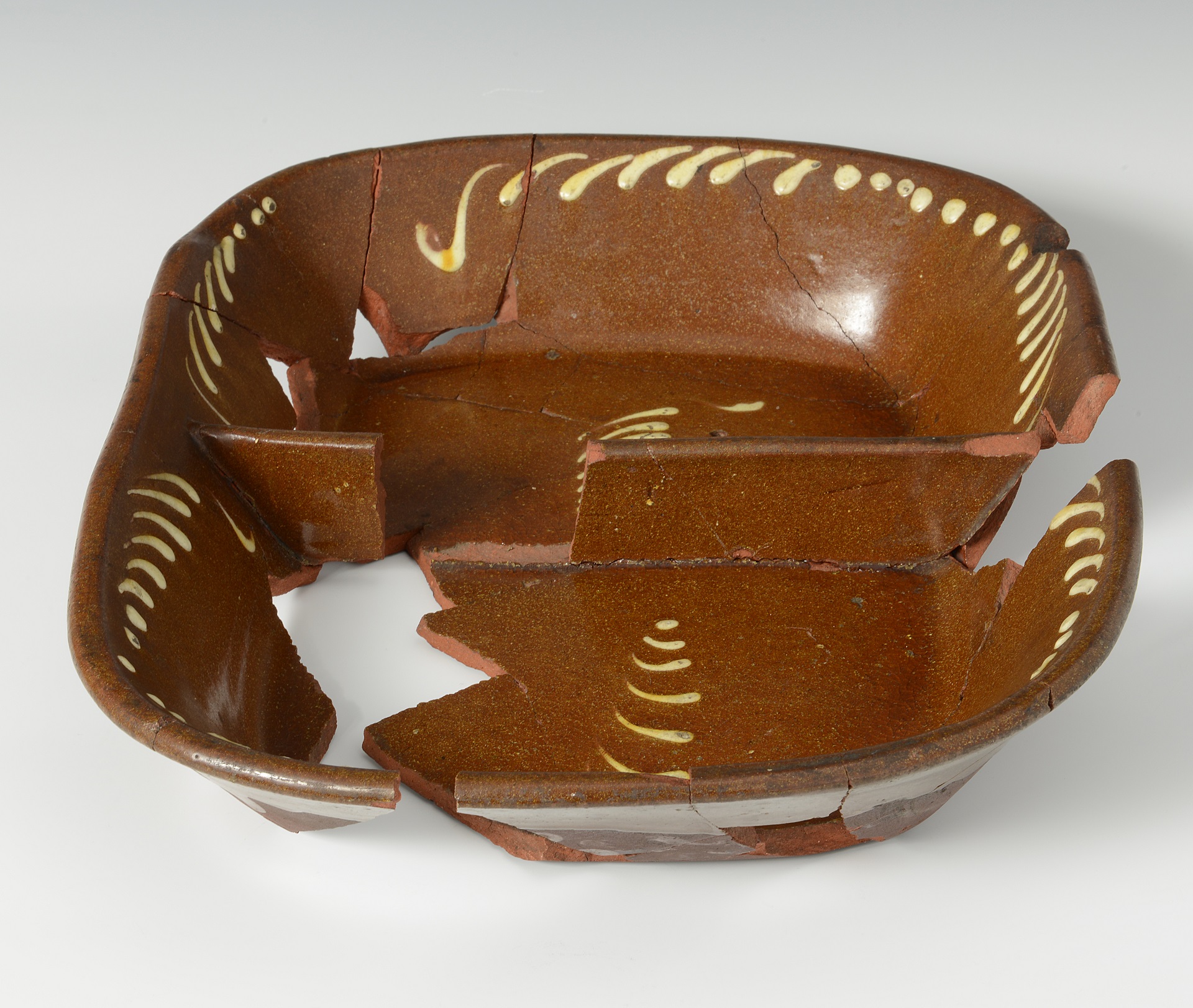 A coloured photograph showing a brown ceramic dish which has been divided into two parts dish which has been reconstructed, there is also yellow decoration along the edge.