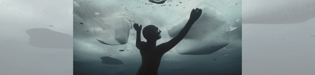 A diver under a sheet of ice reaches for the surface.